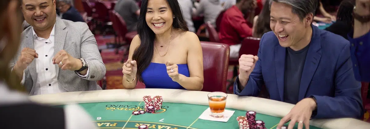 Group of players cheering at an EZ Baccarat table with chips and playing cards in a casino